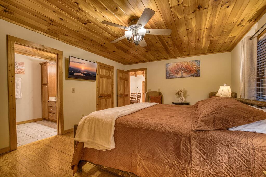 This serene master bedroom features a comfortable king bed adorned with plush bedding and a stylish ceiling fan. A cozy sitting area with a chair offers a perfect spot to relax, while a spacious walk-in closet provides ample storage This serene master bedroom features a comfortable king bed adorned with plush bedding and a stylish ceiling fan. A cozy sitting area with a chair offers a perfect spot to relax, while a spacious walk-in closet provides ample storage - Spacious Cabin, Hot Tub, Theater, Dog Run, FirePit - Ellijay