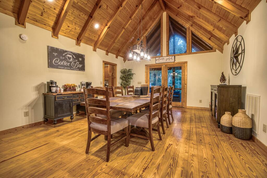 The Bear Necessity's dining area features a 7ft wooden table, seating 8 comfortably, with cozy lighting and woodland decor. A charming coffee bar in the background adds a warm, inviting touch. The Bear Necessity's dining area features a 7ft wooden table, seating 8 comfortably, with cozy lighting and woodland decor. A charming coffee bar in the background adds a warm, inviting touch. - Spacious Cabin, Hot Tub, Theater, Dog Run, FirePit - Ellijay
