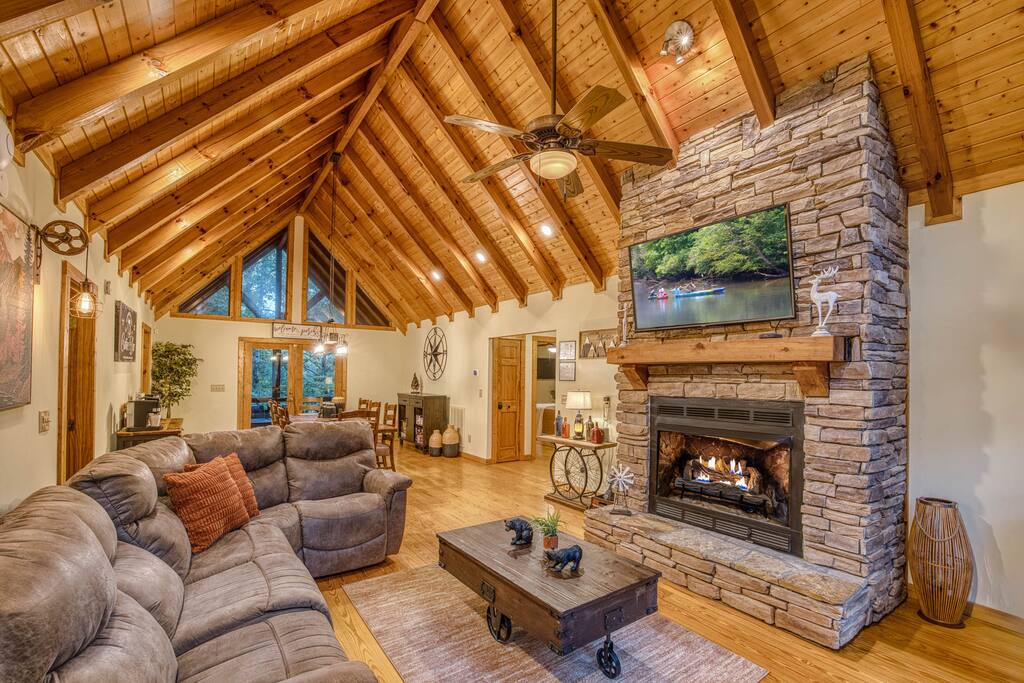 Sink into the cozy sectional couch by the stacked stone gas fireplace and Smart TV. The Vaulted ceilings, natural light, and open-concept design make this the perfect spot to relax. Sink into the cozy sectional couch by the stacked stone gas fireplace and Smart TV. The Vaulted ceilings, natural light, and open-concept design make this the perfect spot to relax. - Spacious Cabin, Hot Tub, Theater, Dog Run, FirePit - Ellijay