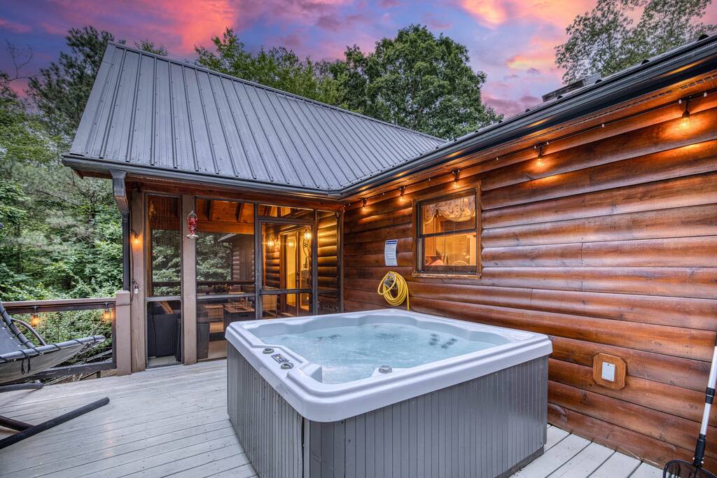 Elevate your getaway with an unforgettable experience on this private deck, featuring a bubbling hot tub where you can soak under a breathtaking sunset sky. Warm string lights cast a magical glow, while a cozy hammock invites relaxation. Elevate your getaway with an unforgettable experience on this private deck, featuring a bubbling hot tub where you can soak under a breathtaking sunset sky. Warm string lights cast a magical glow, while a cozy hammock invites relaxation. - Spacious Cabin, Hot Tub, Theater, Dog Run, FirePit - Ellijay