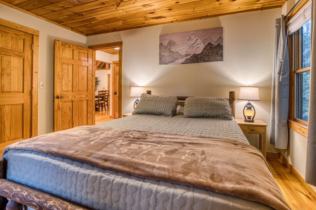 Welcome to the spacious guest bedroom! Featuring a queen-sized luxury mattress, rustic nightstands with lamps, a large closet, Smart TV, and a cozy rocking chair, this room offers the perfect retreat for relaxation and comfort. Welcome to the spacious guest bedroom! Featuring a queen-sized luxury mattress, rustic nightstands with lamps, a large closet, Smart TV, and a cozy rocking chair, this room offers the perfect retreat for relaxation and comfort. - Spacious Cabin, Hot Tub, Theater, Dog Run, FirePit - Ellijay