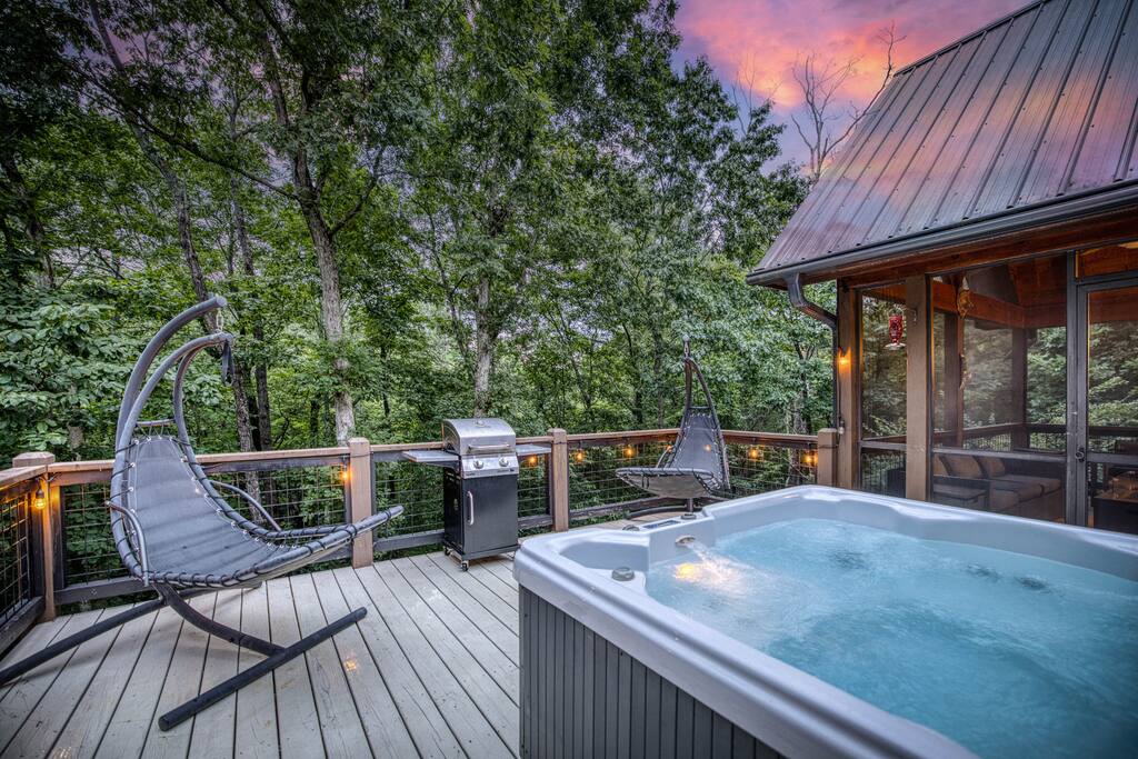 Unwind in the four-person hot tub, illuminated by the soft glow of string lights. Picture yourself enjoying a bottle of wine, creating the perfect setting to sip, soak, and relax in your private retreat. Unwind in the four-person hot tub, illuminated by the soft glow of string lights. Picture yourself enjoying a bottle of wine, creating the perfect setting to sip, soak, and relax in your private retreat. - Spacious Cabin, Hot Tub, Theater, Dog Run, FirePit - Ellijay