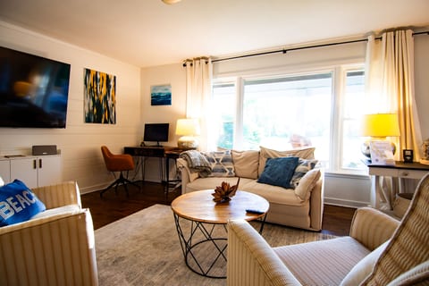 Bright, cozy living room with large windows, TV, and dedicated workspace