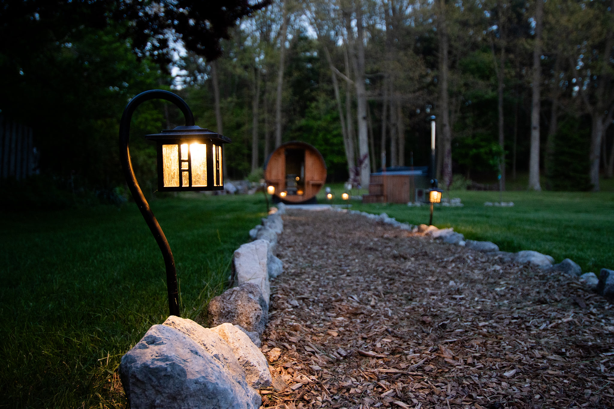 Lit garden path leading to a private sauna and hot tub retreat