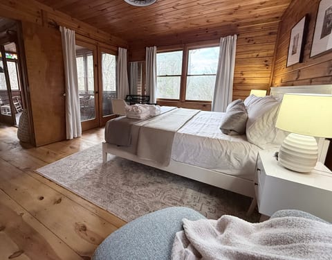 Cozy wood-paneled bedroom with forest views, desk, and screened porch access.