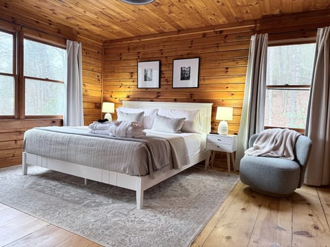 Modern-rustic king suite with forest views, plush linens, cozy chair