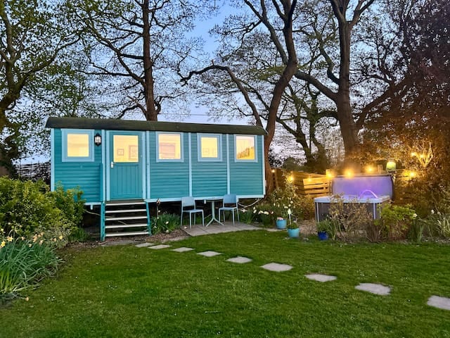 View of Meadowsweet with hot tub and countryside beyond - your own extra-large Shepherd’s hut with a properly plumbed ensuite, electric hot tub and stunning views.

