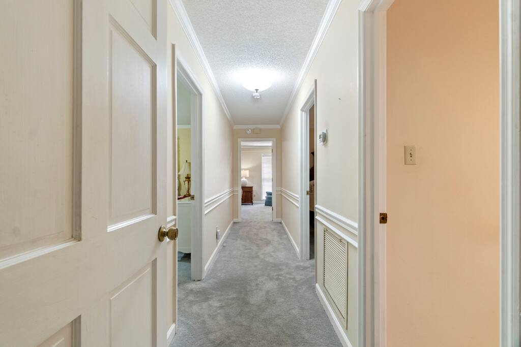 The downstairs hallway leads to three bedrooms, including the spacious main bedroom with a private en-suite at the end of the hall, along with two additional bedrooms that share a full bathroom
