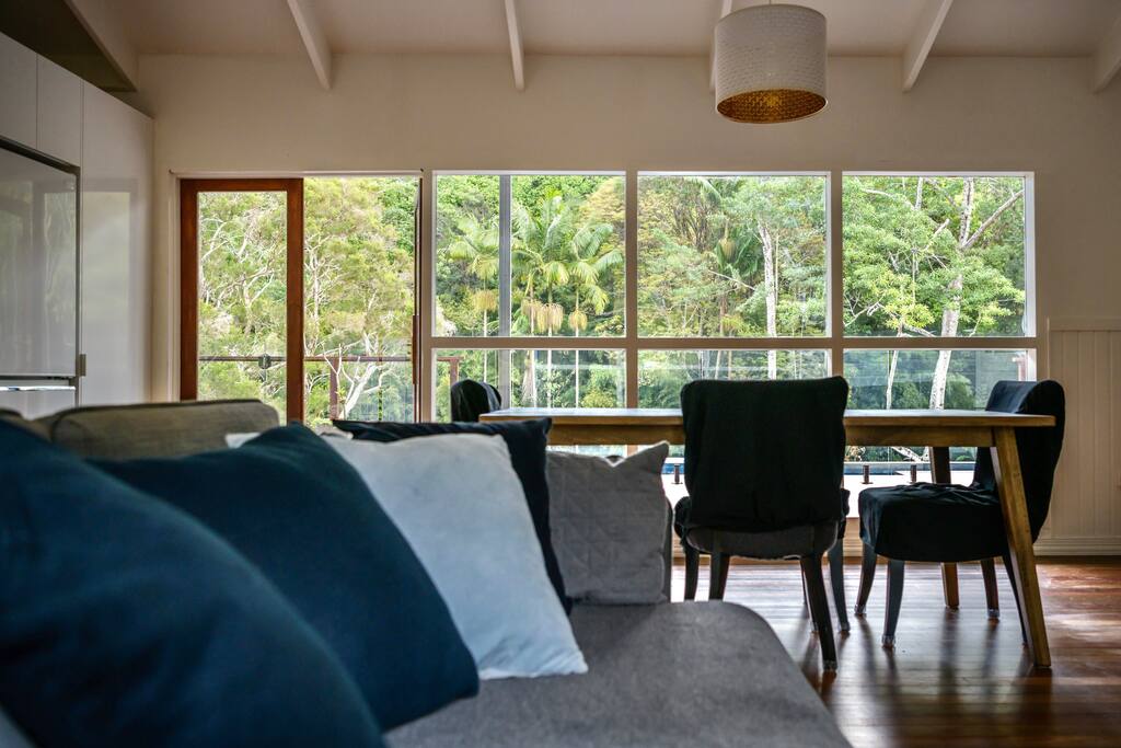 The view from the sofa to the pool side of the house, including the dining table and the windows looking out into the pool and garden beyond, including the creek that you can see from the deck.  