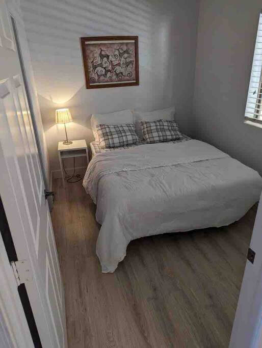 Small Bedroom with queen size bed and attach bathroom with wood floors. 