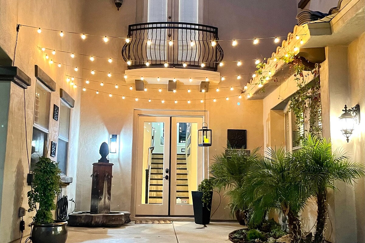 This softly lit courtyard serves as the home’s main entry from the driveway, with café string lights and lush greenery. Guests will use the keypad on the French doors for seamless, secure self check-in and direct access into the home.
