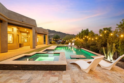 Pool with dinning table and hot tub with string lights near mountain views
