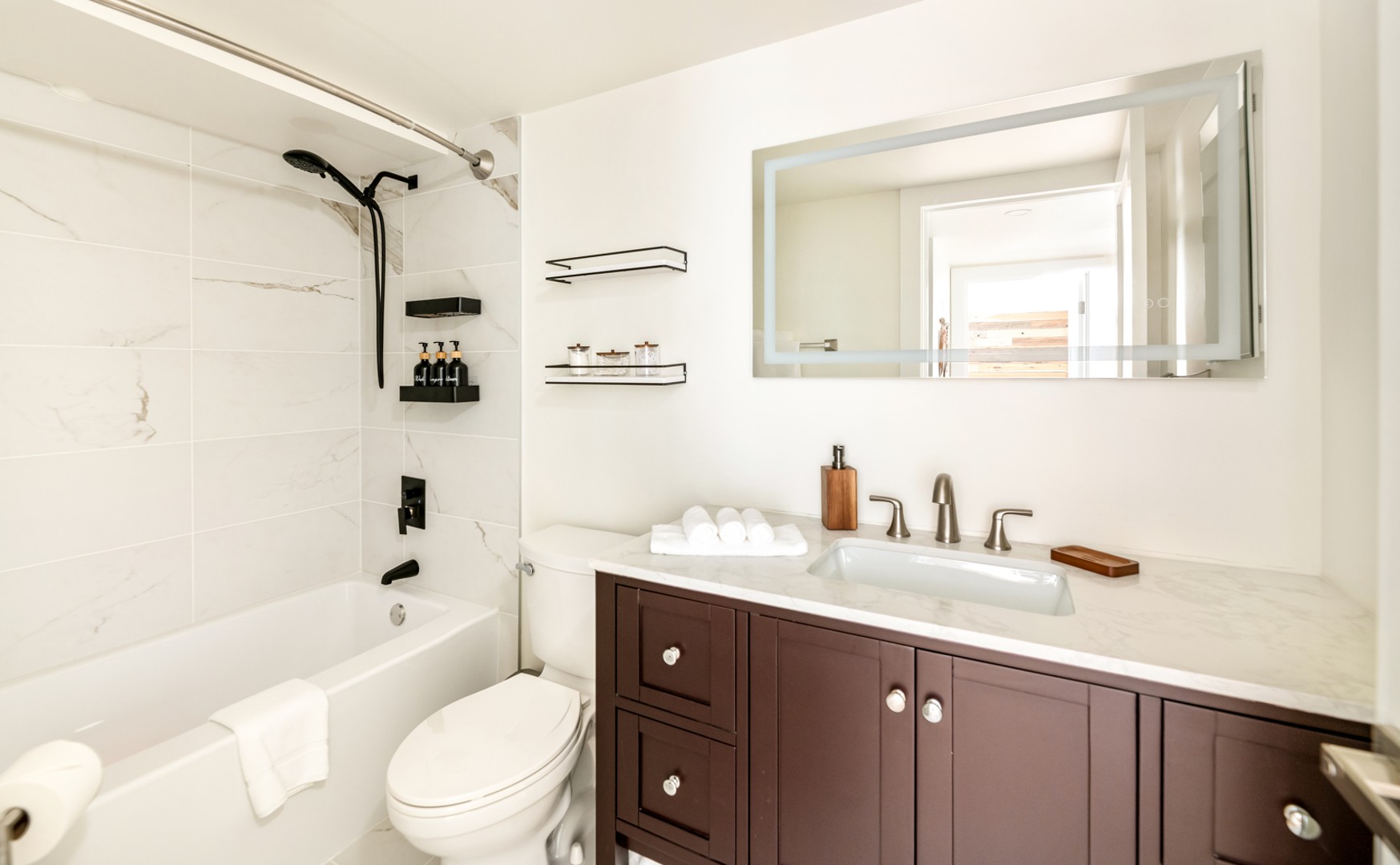 Modern shared bathroom featuring a sleek design with a shower/tub combo, a well-lit vanity, and ample storage