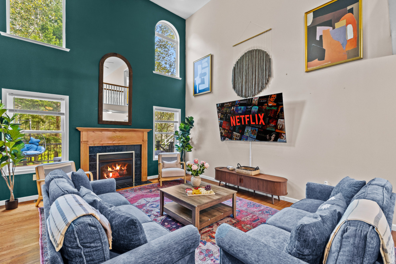 Relax in the spacious living room featuring plenty of seating, a smart TV, a cozy fireplace, and large windows showcasing a beautiful backyard view.