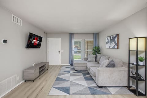 Cozy and modern living room with a plush sectional, Netflix-ready smart TV, and soft natural light from large windows. A perfect space to unwind, complete with sleek floors, stylish decor, and relaxing vibes.
