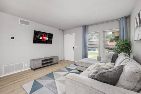 Cozy and modern living room with a plush sectional, Netflix-ready smart TV, and soft natural light from large windows. A perfect space to unwind, complete with sleek floors, stylish decor, and relaxing vibes.