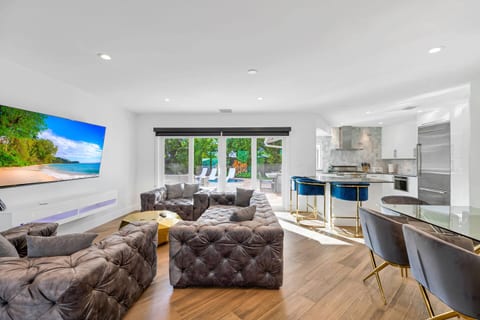 The bright living room offers a cozy atmosphere with plush sofas and a large screen TV, perfect for unwinding after a day by the pool. Natural light fills the space, enhancing the connection to the outdoor area and garden views.