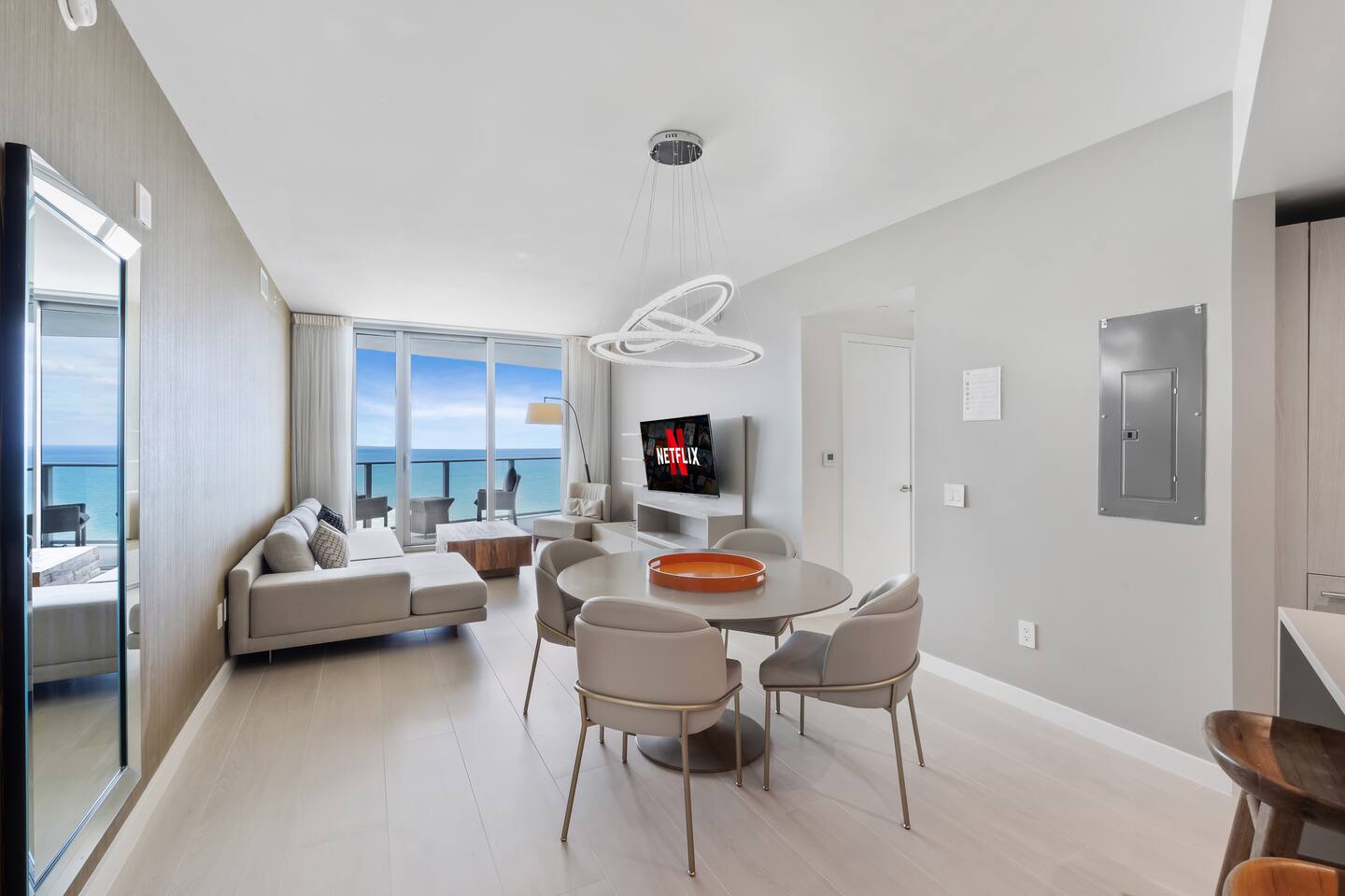 The dining area sits at the center of the open layout, offering a stylish round table and a bright setting for meals with an ocean backdrop.