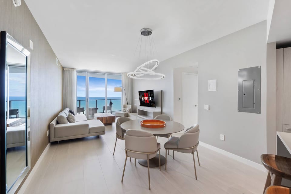 The dining area sits at the center of the open layout, offering a stylish round table and a bright setting for meals with an ocean backdrop.