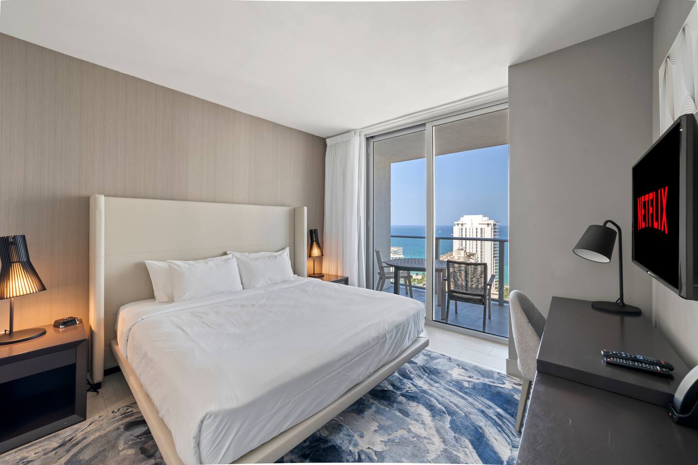 Step into a spacious master bedroom with a king-size bed, bedside tables, and a desk with a convenient lamp. The room opens onto a balcony with seating and ocean views, while the private en-suite bathroom adds comfort and convenience.