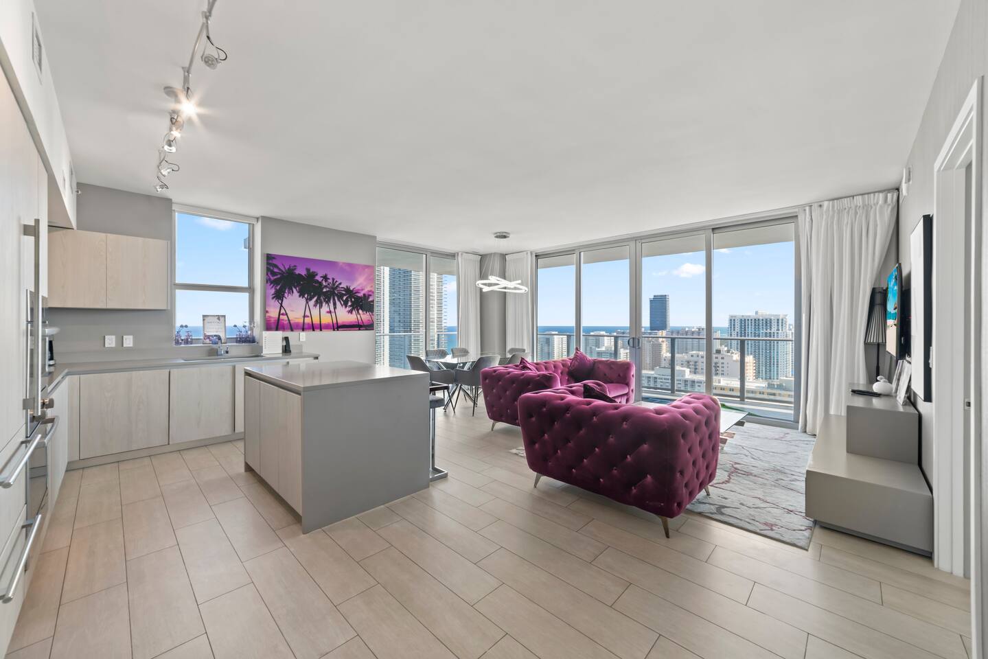 Enjoy an open-plan living space with a sleek kitchen and dining area. Large windows fill the room with natural light and offer expansive city and ocean views, creating a bright and inviting atmosphere for your stay.