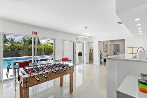 This bright entertainment space features a foosball table and beer pong setup with direct poolside access. Large sliding doors fill the room with natural light, creating a seamless connection between indoor fun and outdoor relaxation.