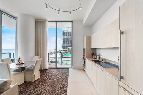 Modern kitchen with sleek cabinetry, built-in appliances, and a spacious countertop. Adjacent dining area features a round table and four chairs with ocean views, making it ideal for cooking and enjoying meals in a bright, open space.
