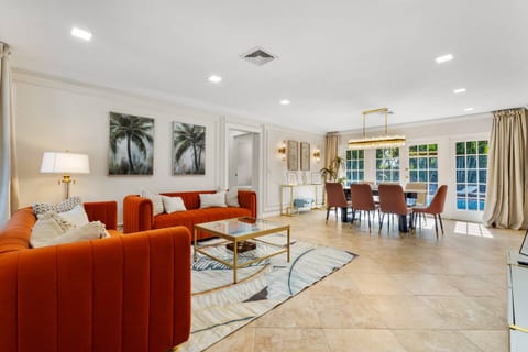The living room extends effortlessly into the dining area, where style meets function. A striking chandelier, elegant furnishings, and views of the poolside patio create the perfect backdrop for memorable meals.
