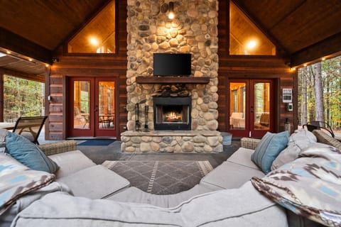 The stunning stone fireplace transforms the covered patio into an outdoor living room with sweeping pine views.
