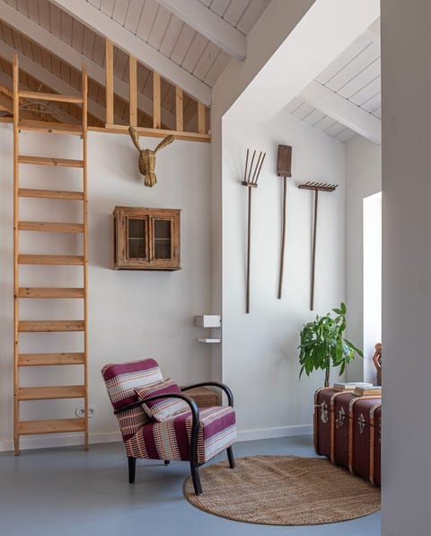 The cosy sitting area is paired with the rustic charm of the ladder leading to the mezzanine, all bathed in sunlight from the expansive window.
