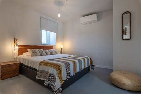 A cosy and bright bedroom with a queen-sized bed, soft tones, and natural light, enhanced by modern touches like air conditioning for comfort