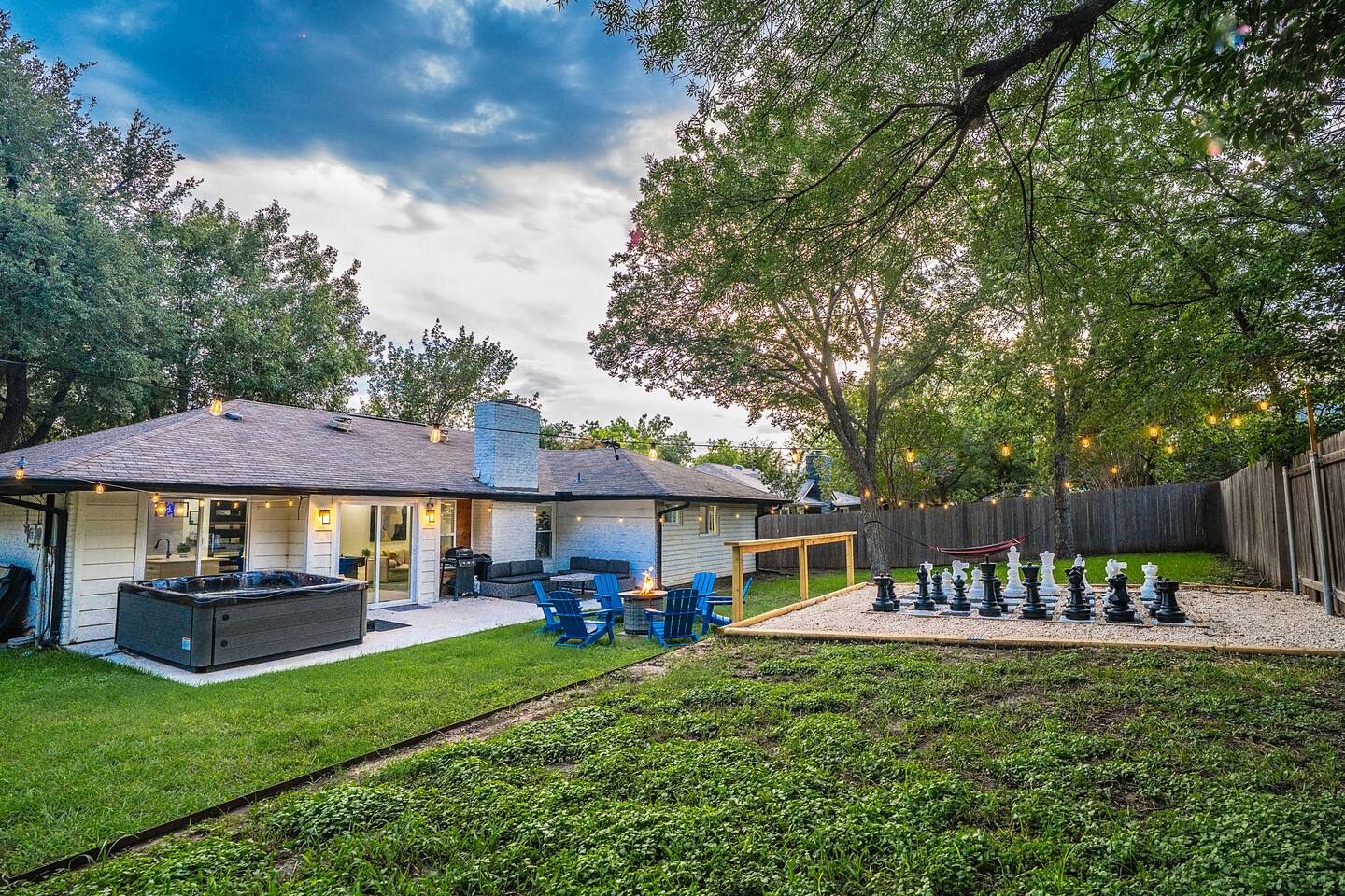 ✨ Spacious backyard retreat featuring a relaxing hot tub, cozy fire pit lounge, BBQ and giant outdoor chess set,  perfect for fun evenings under the string lights.