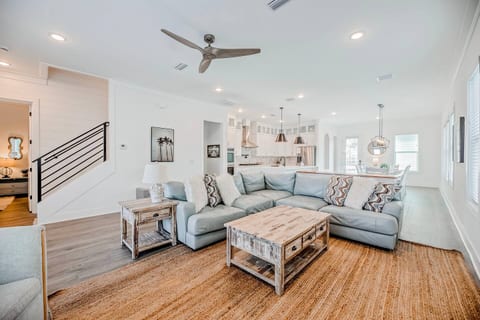 Bright and airy living room with oversized sectional, coastal decor, and seamless flow to the kitchen and dining area. Ideal for large groups and family time.