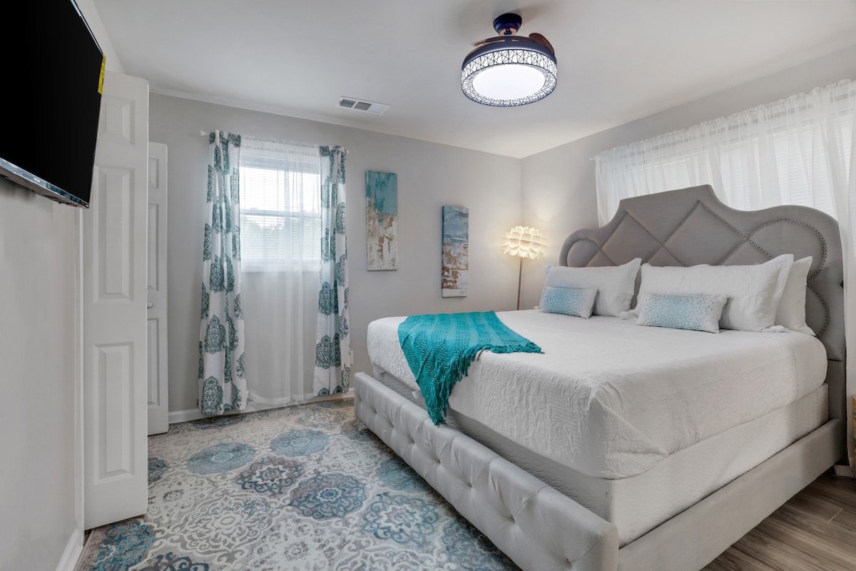 Our master ensuite, features a king bed, pack 'n play in the closet, a night lamp, hangers,  side tables with extra plugs and usb ports for nighttime charging, a luggage holder, and a private bathroom, all set in a refreshing teal decor.