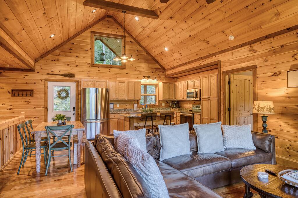 Main floor entrance to cabin has large open concept space with vaulted ceilings trimmed beautifully with natural stained wood and a stone fireplace. True modern rustic vibe, this space is great for everyone to gather 