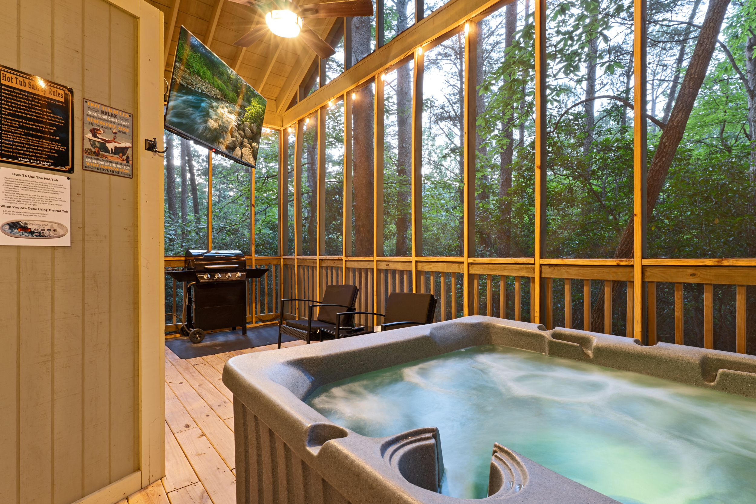 Unwind in the private hot tub surrounded by nature. Your screened-in porch includes cozy seating, a grill, and a mounted TV — perfect for relaxing rain or shine.