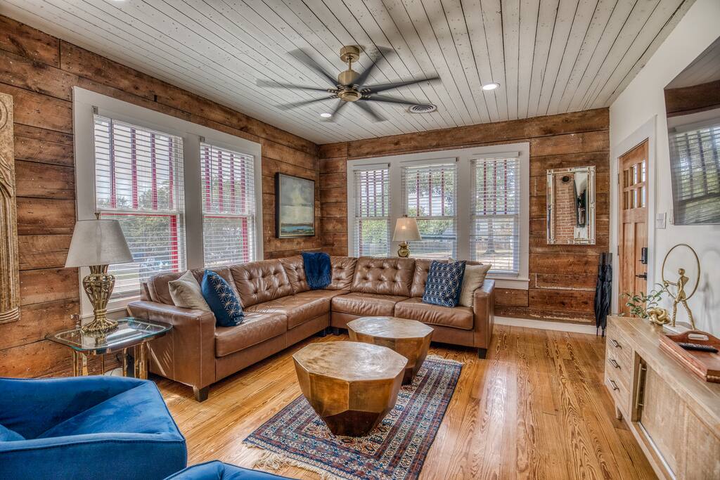 Stylish industrial-style living room with antique wood slat walls, exposed brick, and warm wood floors. Relax in comfort with cozy seating and modern amenities and a 70" TV! Perfect for your next Airbnb stay in downtown Brenham!
