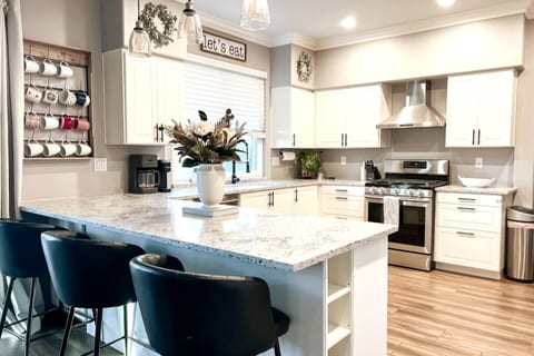 Chef's kitchen with 5-burner gas stove and oven, stainless steel vent hood, quartz countertops and peninsula with breakfast bar seating. Well equipped with cookware, appliances, and dishes for serving a home-cooked or restaurant-delivered meal.
