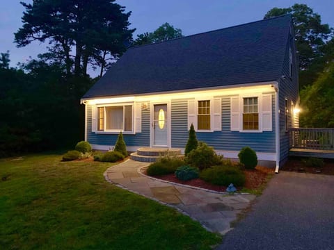 Charming exterior with lush greenery and welcoming lighting, your Cape Cod vacation haven from the moment you arrive.