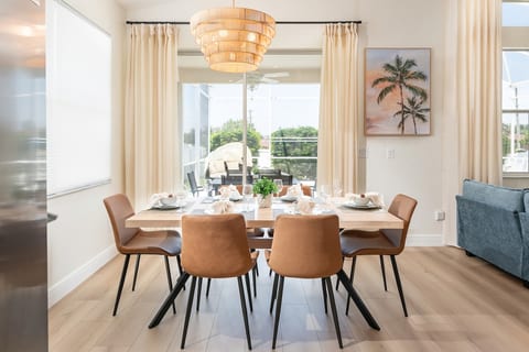 Gather in a tropical organic-modern dining space with serene views of the pool, open living room, and kitchen—perfect for shared meals and memories.