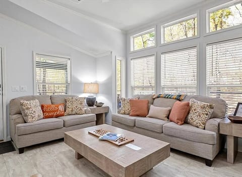 Bright, airy living room with large windows, cozy seating, and serene forest views. A perfect space to relax, read, or gather with loved ones.