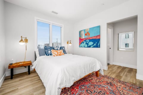 Bright bedroom with queen bed, artwork, and city views