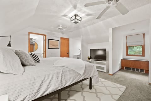 Upstairs primary bedroom with king bed, TV, and ceiling fan