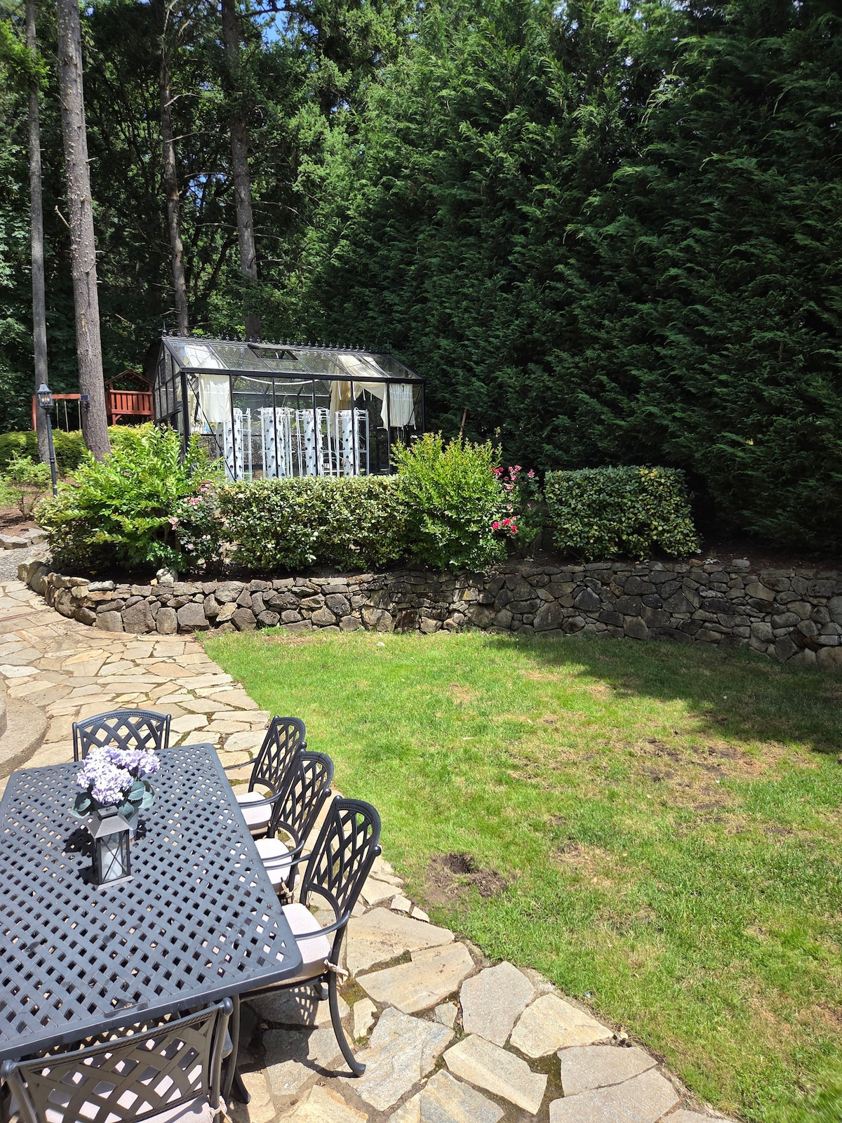 Outdoor patio with flagstone, dining for 8, 40-ft Leyland cypress trees for privacy, greenhouse, and rock retaining walls. Located just off the kitchen and main living room.
