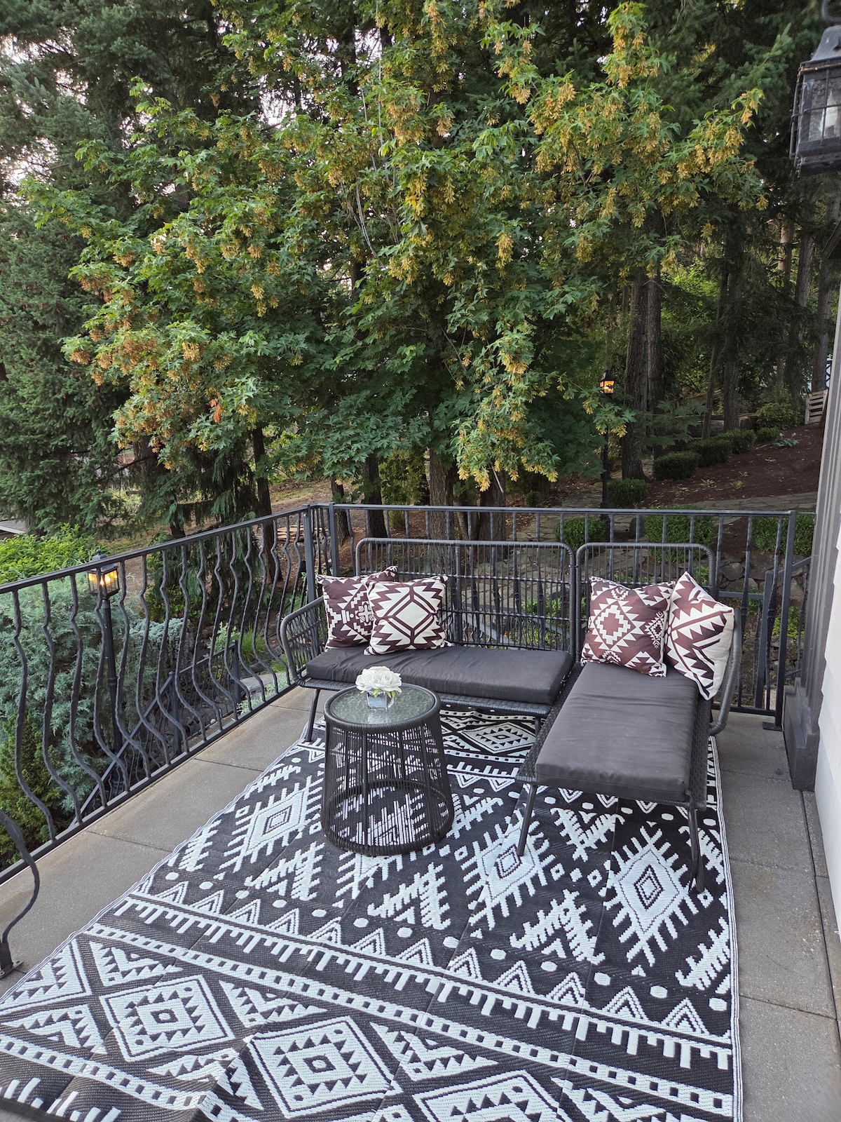 Private balcony off the front of the house with wrought iron railing, treetop views, and a cozy seating area overlooking flagstone paths, pond, and waterfall.