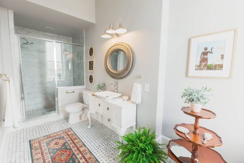 Bathroom attached to Bedroom 1 features marble tile and custom white pedestal vanity with antique tiered dumbwaiter accent