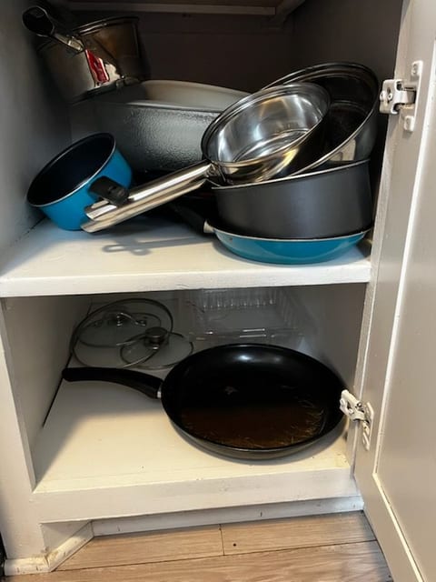 Well-stocked kitchen cabinet with pots, pans, and cooking essentials