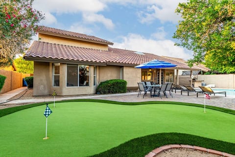 Enjoy backyard fun with this spacious putting green and seating area under a vibrant blue umbrella—great for morning practice or afternoon games with friends.