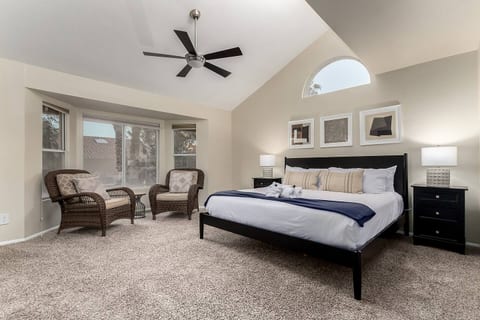 Unwind in a luxurious king bed beneath vaulted ceilings with wicker lounge chairs, stylish nightstands, and plush carpet for ultimate relaxation.