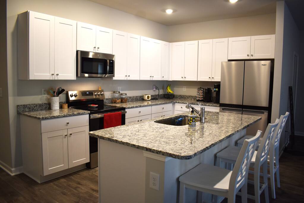 Modern kitchen with granite counters, stainless steel appliances, and island seating — fully stocked for home-cooked meals and perfect for entertaining during your stay.